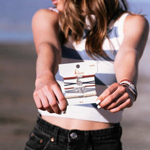 Load image into Gallery viewer, Girl at the beach holding and wearing the Small Brave K&#39;lani hair tie and bracelet around her wrist.
