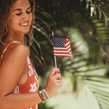 Load image into Gallery viewer, Girl smiling holding the American flag wearing the small K&#39;lani hair tie and bracelet around her wrist.
