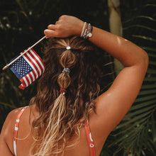 Load image into Gallery viewer, Girl holding the American Flag and wearing the small Brave K&#39;lani hair tie and bracelet in her hair and around her wrist.
